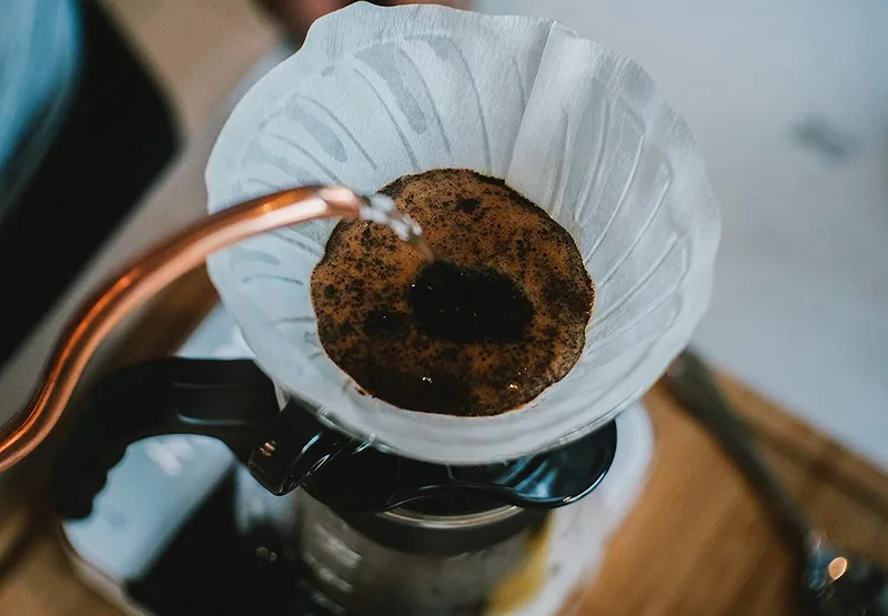 Hot water from a gooseneck kettle drips through ground coffee in a paper pour-over cone